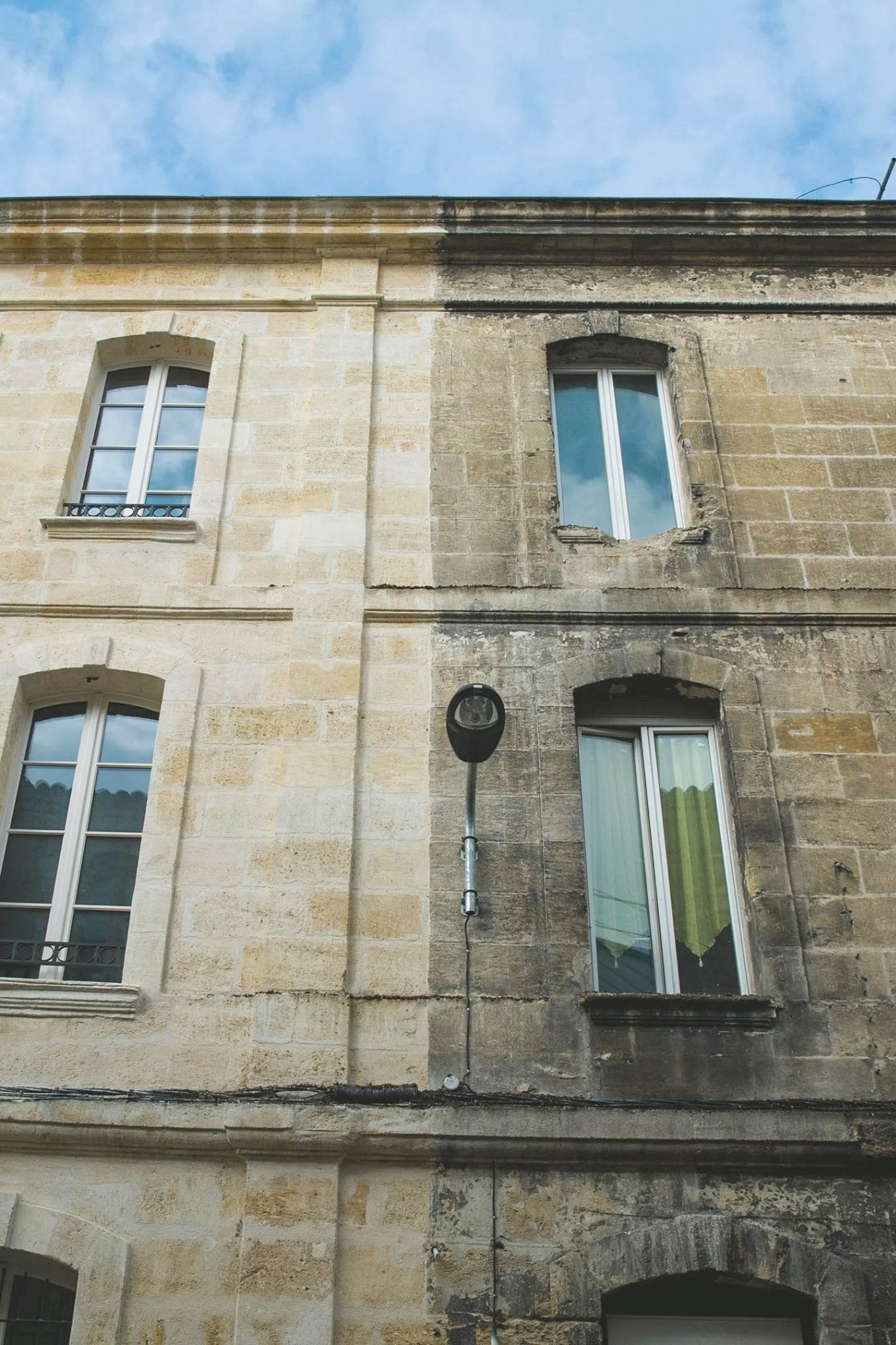 Elewacja budynku w trakcie czyszczenia: lewa strona odnowiona, ukazująca jaśniejszy kamień, kontrastująca z brudną, ciemniejszą prawą stroną.