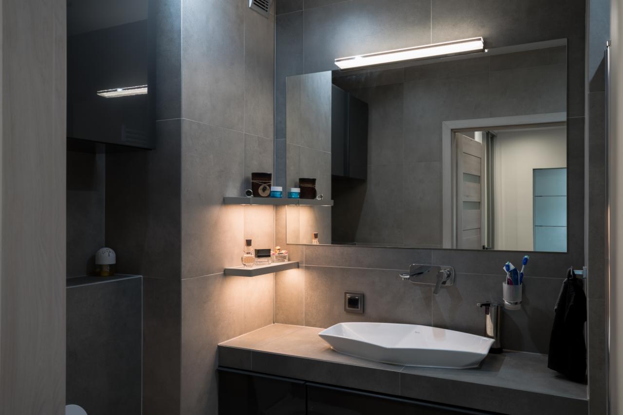 Nowoczesna łazienka w odcieniach szarości z podświetlanymi półkami, designerską umywalką i dużym lustrem.