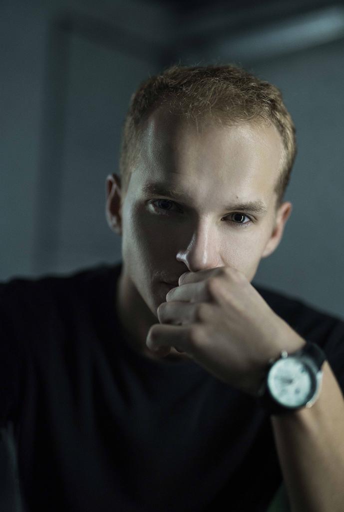 Portret młodego mężczyzny z zegarkiem na ręce, w stonowanej tonacji, wykonany przez fotografa z Krakowa.