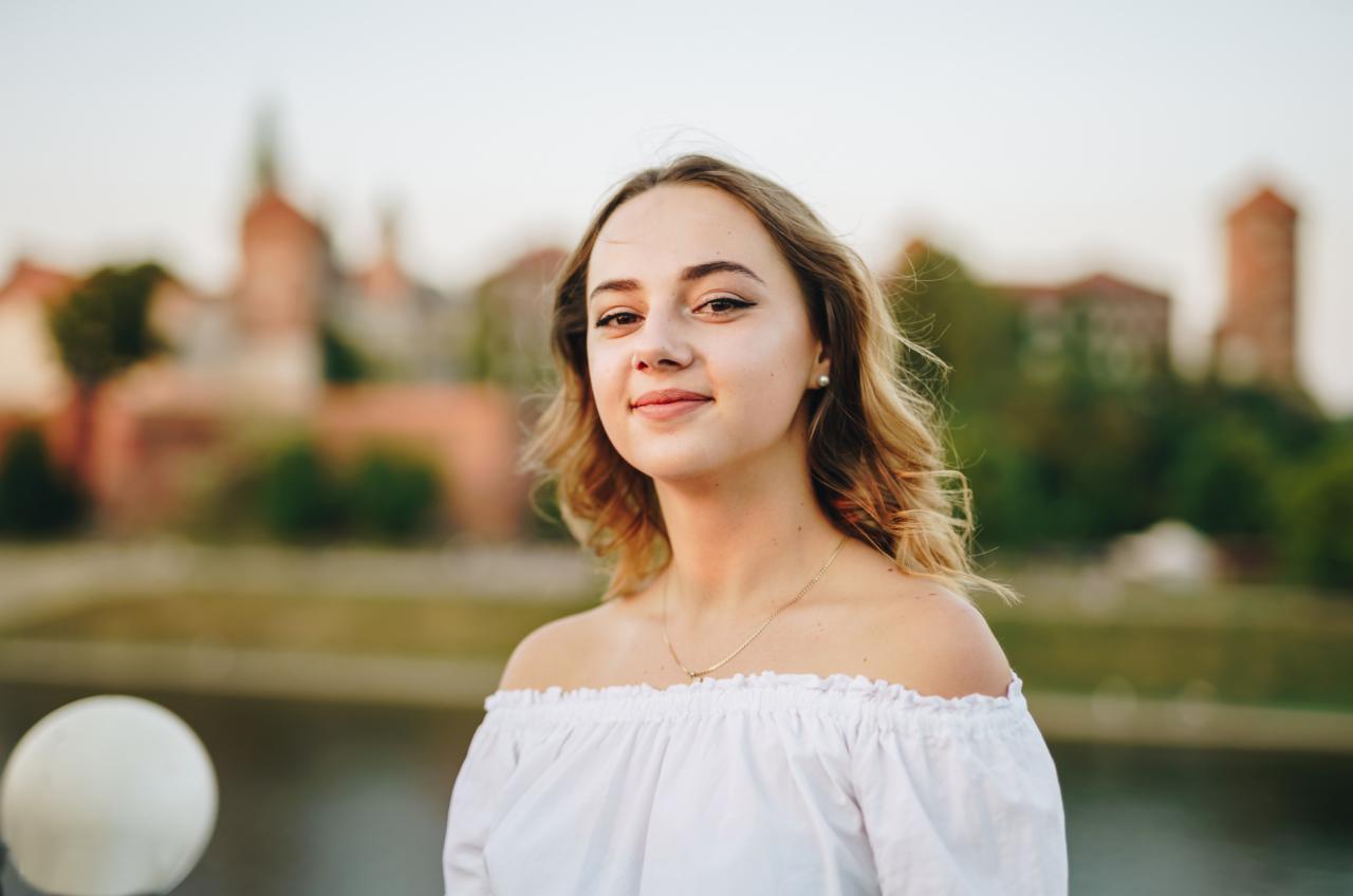 Portret kobiety w białej bluzce z odkrytymi ramionami na tle krakowskiego Wawelu, wykonany podczas sesji zdjęciowej na zewnątrz.
