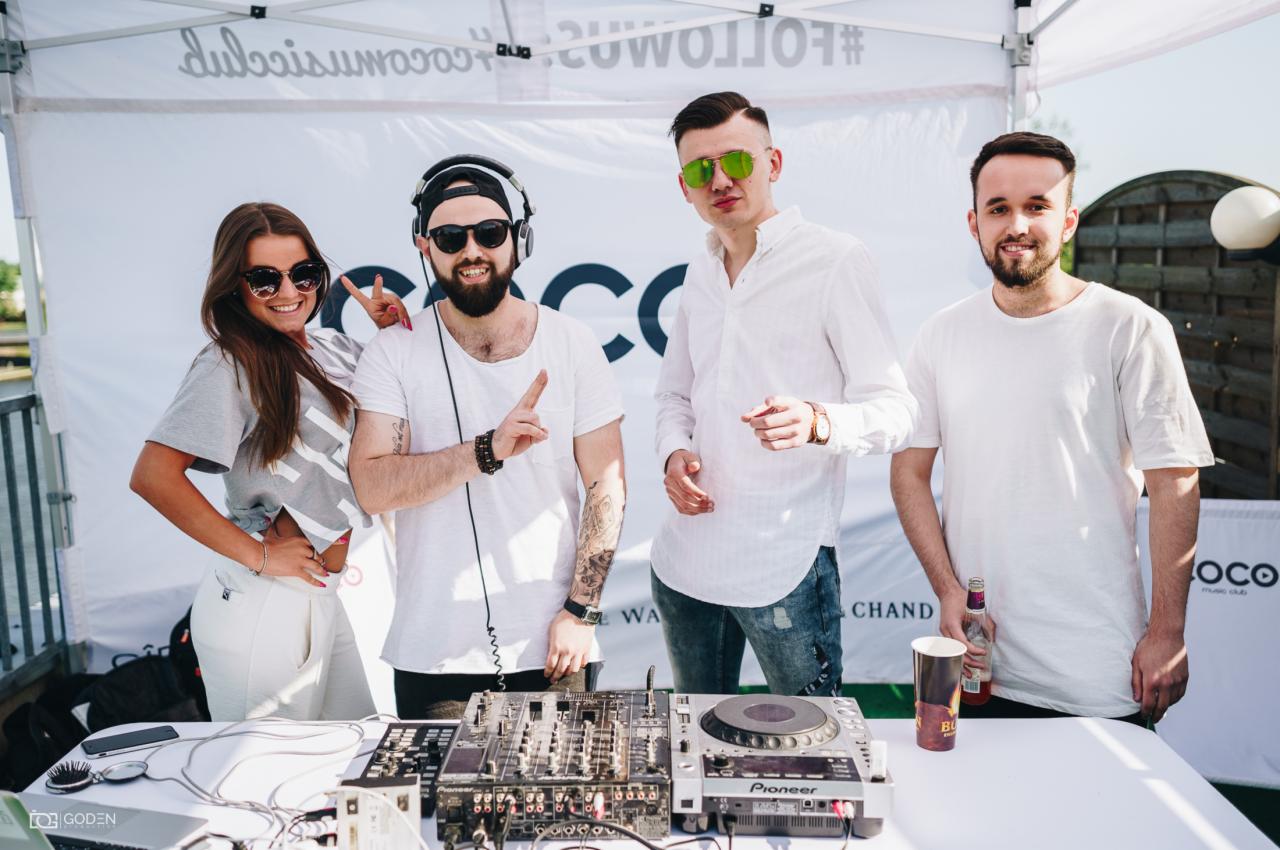 Grupa czterech osób, w tym DJ z profesjonalnym sprzętem Pioneer, pozuje na tle białego namiotu z logo Coco Music Club i hasłem #FOLLOWCOCO, podczas imprezy plenerowej.