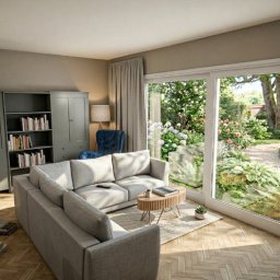 Przedsiębiorstwo Budowlane Limax Sp. z o.o. - Jasne wnętrze salonu z szarą sofą narożną, regałem na książki i widokiem na ogród przez duże okno przesuwne. Parkiet w jodełkę na podłodze.