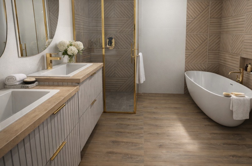 Nowoczesna łazienka z drewnopodobną podłogą i ścianami, białą wanną wolnostojącą i szafką z umywalkami. Kabina prysznicowa ze złotymi ramami.
