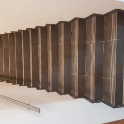 Wykończone schody z ciemnej, pionowo ułożonej glazury z jasnymi fugami w Grądy-Woniecko, widok z góry na całą długość biegu, z zamontowaną metalową poręczą.