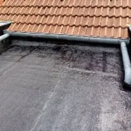 Czarna, płaska powierzchnia dachu po hydroizolacji w Cychrach, z widocznymi rynnami i fragmentem dachu z czerwonej dachówki w tle.