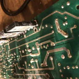 Zbliżenie na zieloną płytę drukowaną z elementami elektronicznymi, lutowane połączenia, widoczne ślady topnika i zabrudzenia.