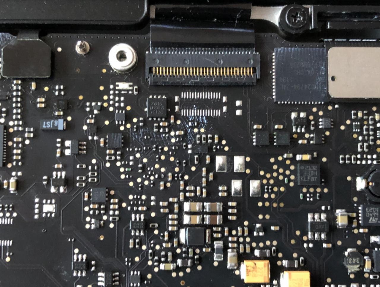 Zbliżenie na czarną płytę główną laptopa z widocznymi elementami elektronicznymi, układami scalonymi i złączami. Widoczne ślady po czyszczeniu.