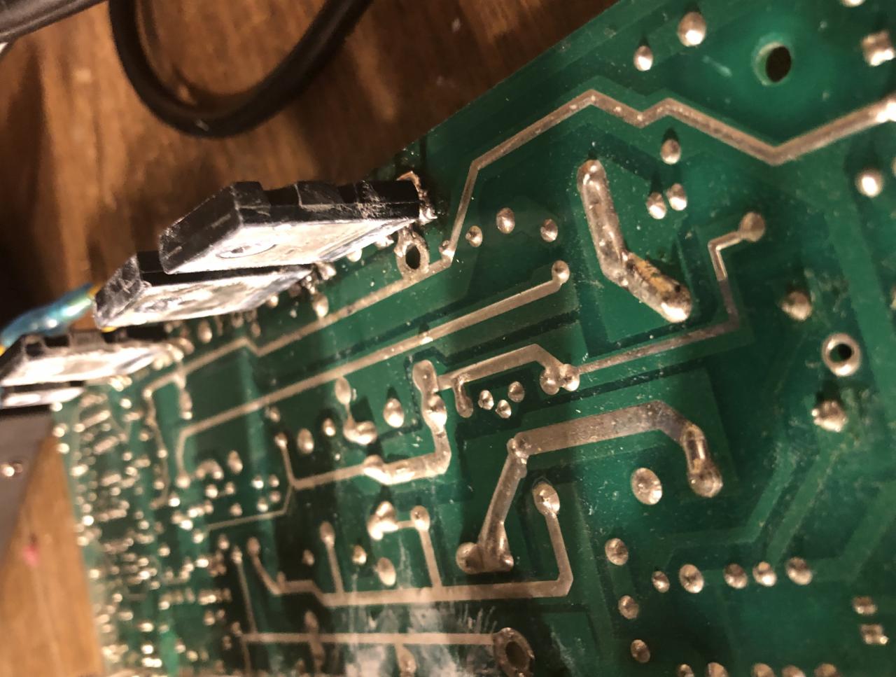 Zbliżenie na zieloną płytę drukowaną z elementami elektronicznymi, lutowane połączenia, widoczne ślady topnika i zabrudzenia.