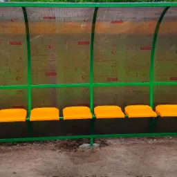 Przystanek autobusowy z zieloną metalową konstrukcją i pomarańczowymi siedzeniami w Poćwiardowie, z przezroczystym zadaszeniem z nadrukiem.