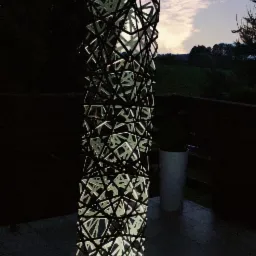 Nowoczesna, podświetlana konstrukcja o ażurowym wzorze na tarasie, z widokiem na zachodzące słońce i zieleń w tle.