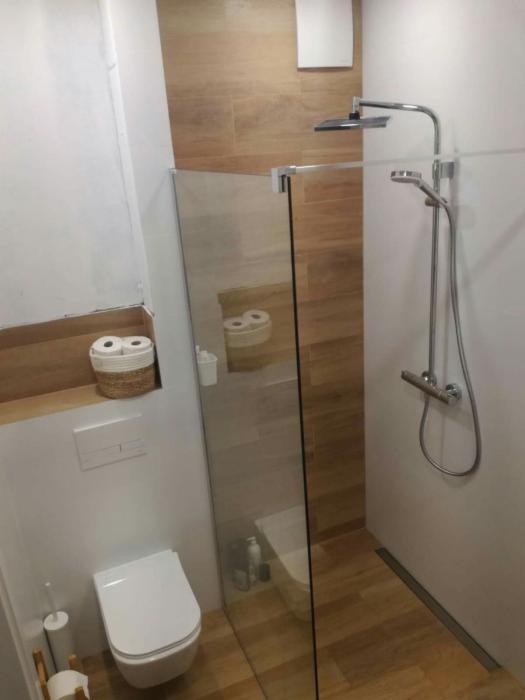 Nowoczesna łazienka z kabiną prysznicową typu walk-in, drewnopodobnymi płytkami, podwieszaną toaletą i deszczownicą z dodatkową słuchawką.