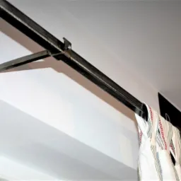 Metalowy karnisz przymocowany do ściany za pomocą wspornika, z zawieszonymi zasłonami w paski.