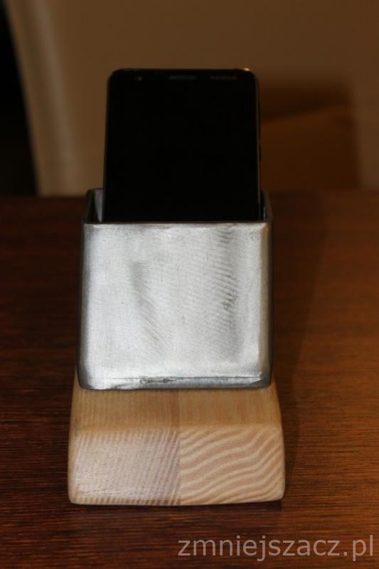 Metalowy, spawany uchwyt na telefon komórkowy z drewnianą podstawą, ustawiony na drewnianym stole.