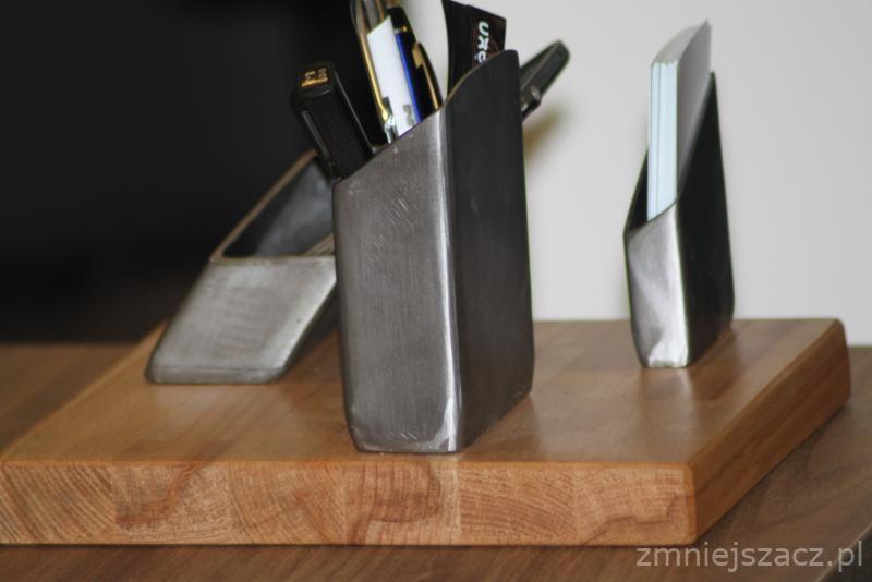 Metalowe przyborniki biurowe spawane na drewnianej podstawie, widoczne ślady obróbki metalu.