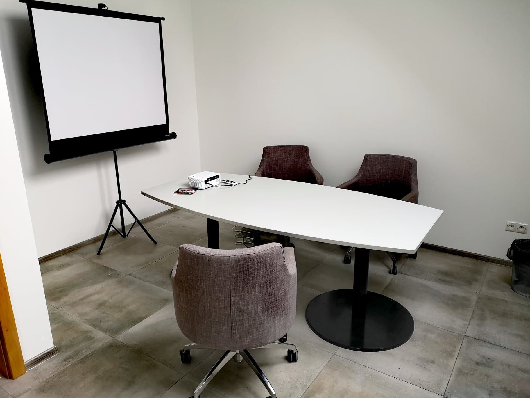 Sala konferencyjna z projektorem, ekranem i owalnym stołem, przygotowana do prezentacji.