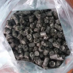 Worek wypełniony ciemnym agropelletem o nieregularnej powierzchni, widoczne ślady pyłu i drobne pęknięcia.