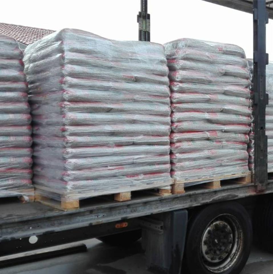 Załadowana ciężarówka z paletami worków, owiniętych folią, prawdopodobnie z materiałem opałowym, widoczne opony i konstrukcja ciężarówki.