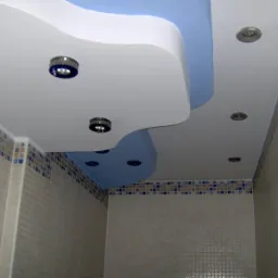 Sufit podwieszany w łazience z oświetleniem punktowym i niebieskim akcentem, wykończony mozaiką.