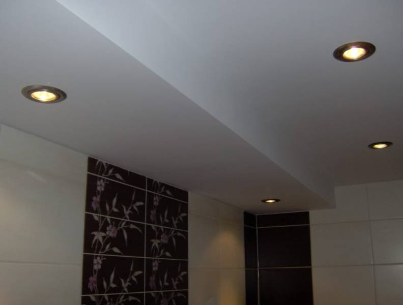 Biały sufit podwieszany z wbudowanymi, okrągłymi lampkami halogenowymi w łazience z brązowo-białymi płytkami z motywem kwiatowym.