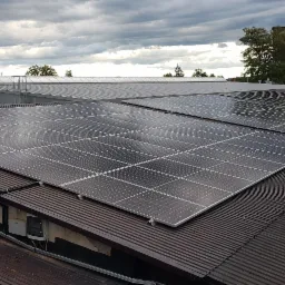 Instalacja fotowoltaiczna 50 kWp na dachu przemysłowym z blachy trapezowej, widoczne moduły skierowane w stronę pochmurnego nieba.