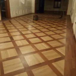 Parkiet po renowacji z widocznymi śladami szlifowania i odkurzaczem przemysłowym w przestronnym wnętrzu z dekoracyjnymi listwami ściennymi.