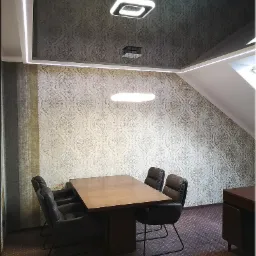 Nowoczesne biuro z ciemnym, wzorzystym sufitem podwieszanym, oświetlonym listwami LED i designerskimi lampami wiszącymi nad drewnianym stołem i skórzanymi krzesłami.