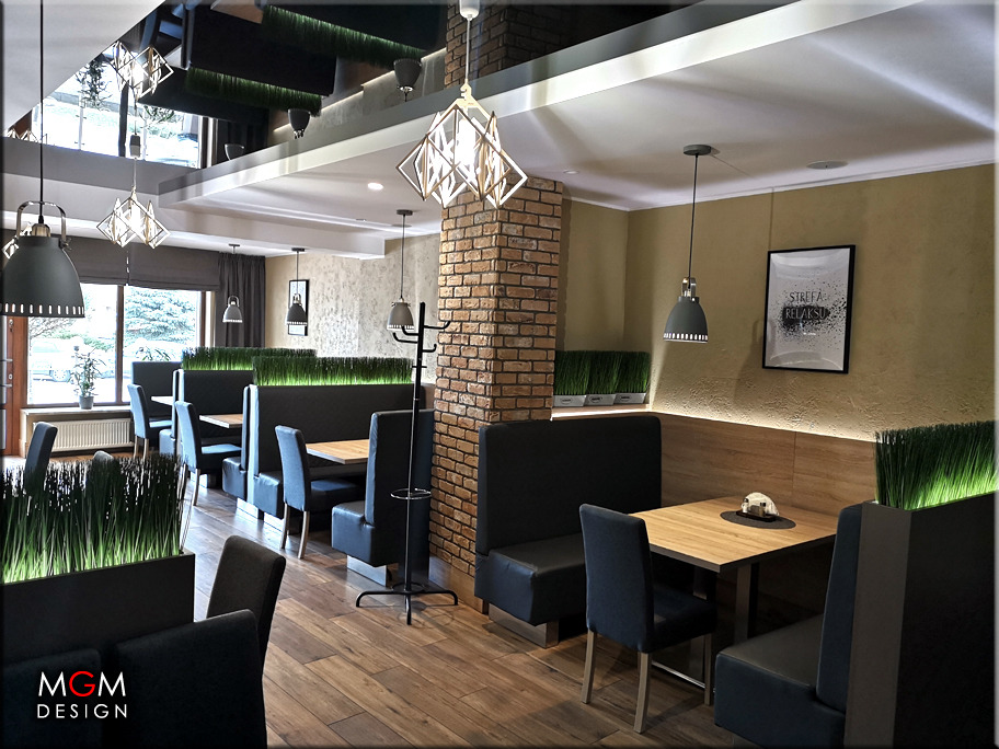 Wnętrze restauracji z drewnianymi stołami, czarnymi lożami i krzesłami, ceglanym filarem i dekoracyjnym oświetleniem.