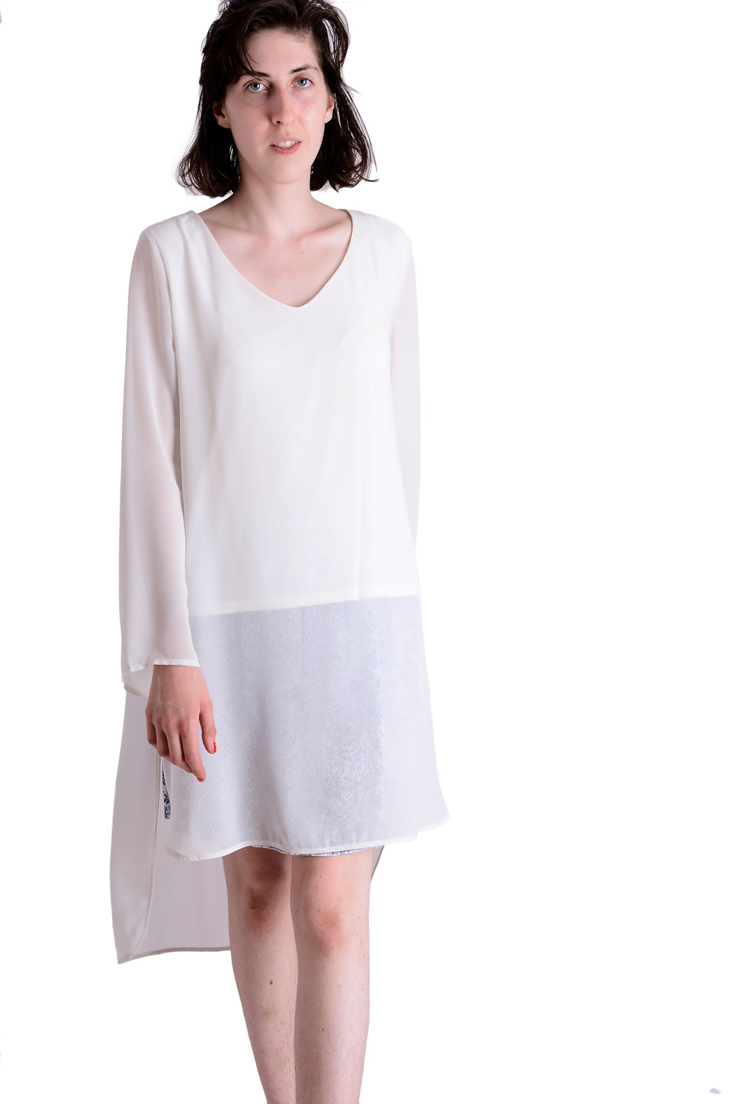 Portret kobiety w białej, asymetrycznej tunice z długimi, prześwitującymi rękawami, na białym tle.