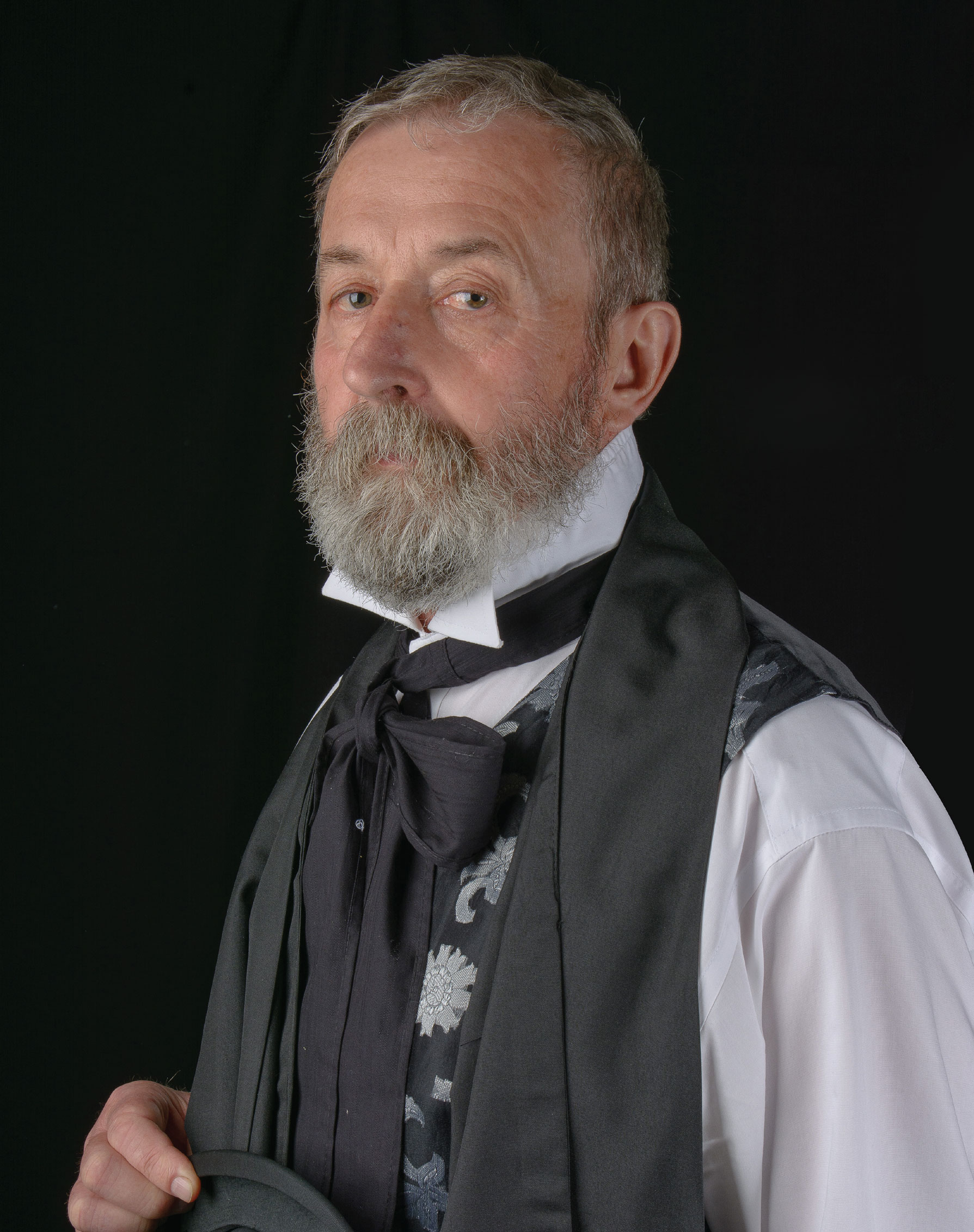 Portret mężczyzny z brodą w stroju z epoki, na czarnym tle, trzymającego kapelusz.