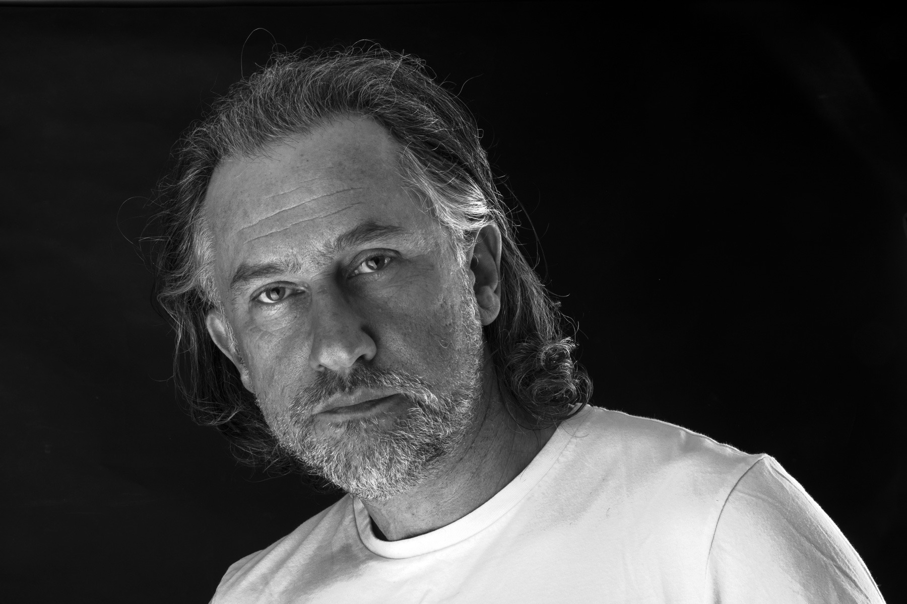 Czarno-biały portret mężczyzny z brodą, skierowany lekko w dół, na ciemnym tle.