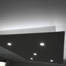 Sufit podwieszany z oświetleniem punktowym, widok z dołu, szare ściany i biały sufit, fragment okna po lewej stronie.