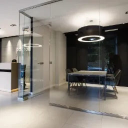 Nowoczesne biuro z przeszkloną ścianą działową, recepcją z logo 'payroll' i minimalistycznym oświetleniem, widok na salę konferencyjną z czarnymi krzesłami i oknem.