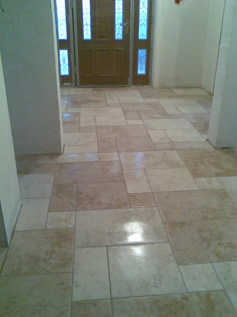 Beżowa podłoga z płytek o zróżnicowanych wymiarach ułożona w korytarzu, widoczna drewniana brama wejściowa z szybkami.