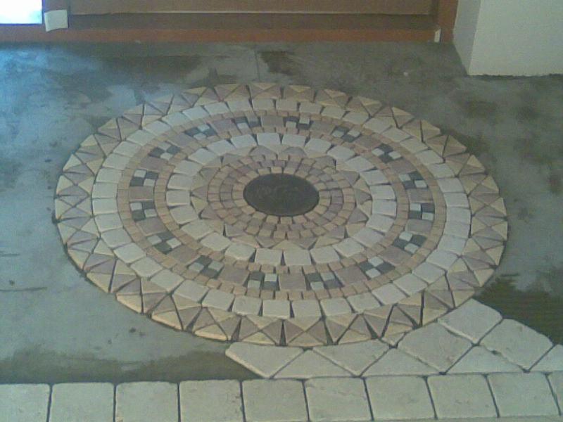 Układanie mozaiki z płytek o różnych kształtach w okrągły wzór na podłodze, widoczne niedokończone brzegi i fragmenty zaprawy.
