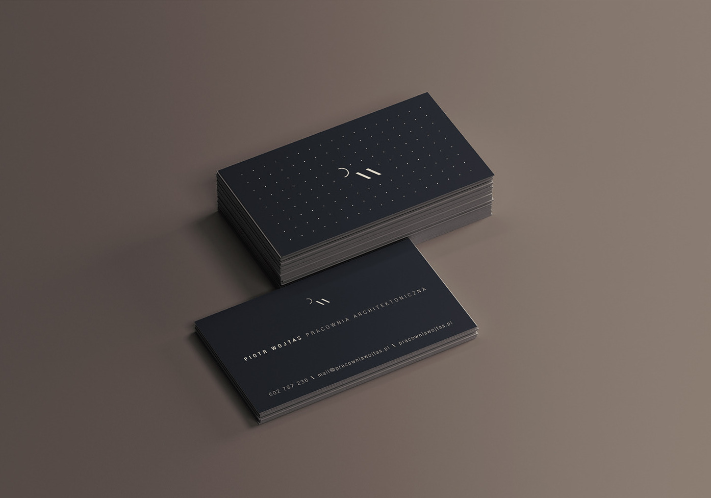 Wizytówki architektoniczne Piotra Wojtasa z minimalistycznym logo i danymi kontaktowymi ułożone na gładkim, beżowym tle.
