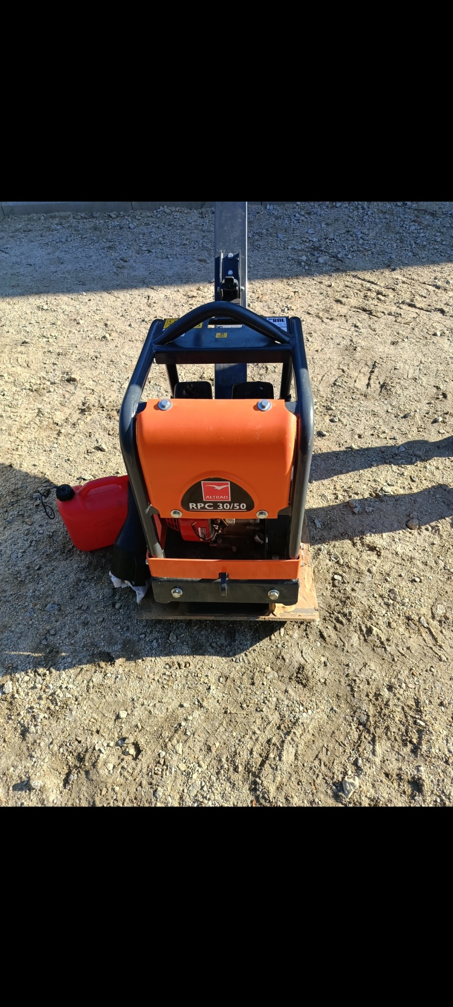 Pomarańczowa zagęszczarka gruntu Altrad RPC 30/50 na ziemistym podłożu. Widoczny kanister z paliwem. Sprzęt budowlany gotowy do pracy na placu budowy.