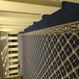 Długi korytarz w hotelu z ciemną wykładziną w złote wzory, widok z góry na okna po lewej stronie.