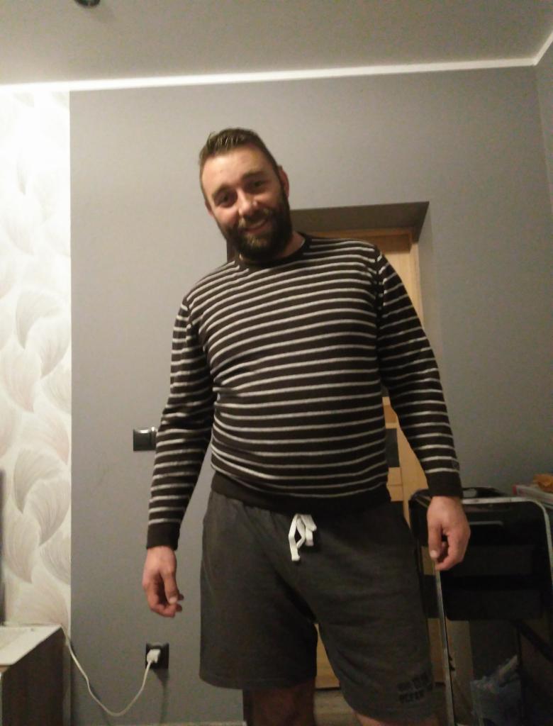 Mężczyzna w paski w szortach, stojący w szarym biurze przed drzwiami i gniazdkiem elektrycznym.