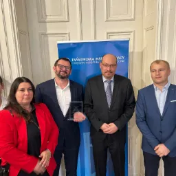 Grupa osób pozuje do zdjęcia z nagrodą PIP „Buduj bezpiecznie” na tle baneru Państwowej Inspekcji Pracy.