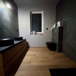 MHM Marta Wypych - Nowoczesna łazienka z czarnymi elementami wyposażenia, drewnianą podłogą i ścianami wykończonymi płytkami imitującymi marmur. Umywalki nablatowe i wisząca toaleta.