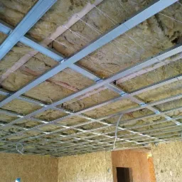 Montaż metalowego stelażu sufitowego z izolacją z wełny mineralnej, widoczne przewody elektryczne, ściany wykończone płytami OSB.