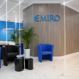 Recepcja firmy Emiro z niebieskimi i czarnymi fotelami, roślinami doniczkowymi i podświetlanymi panelami ściennymi.