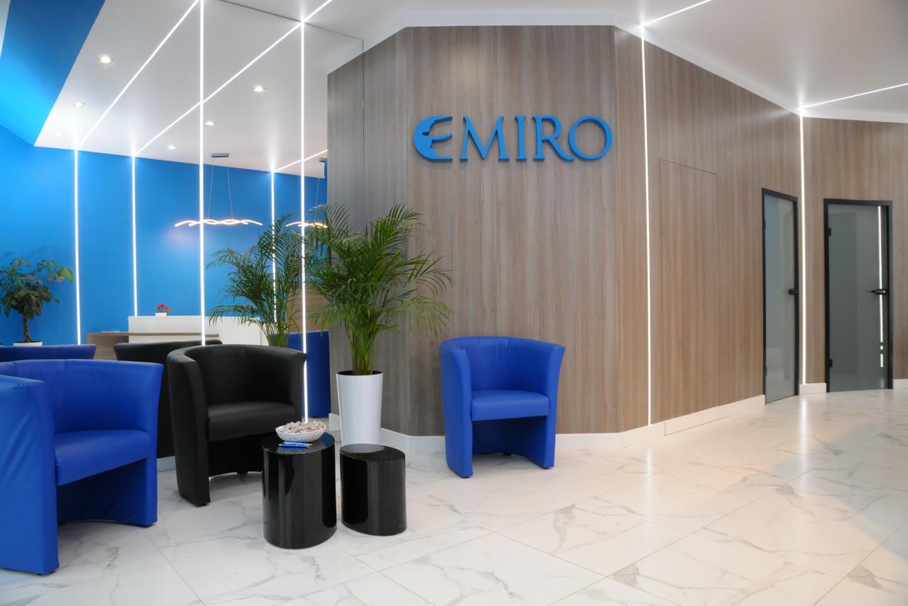 Recepcja firmy Emiro z niebieskimi i czarnymi fotelami, roślinami doniczkowymi i podświetlanymi panelami ściennymi.