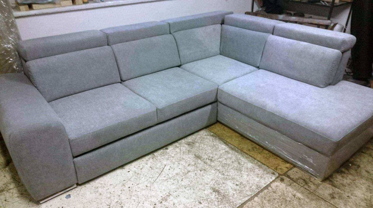 Szary narożnik z regulowanymi zagłówkami, częściowo owinięty folią ochronną, na posadzce z widocznymi śladami użytkowania.