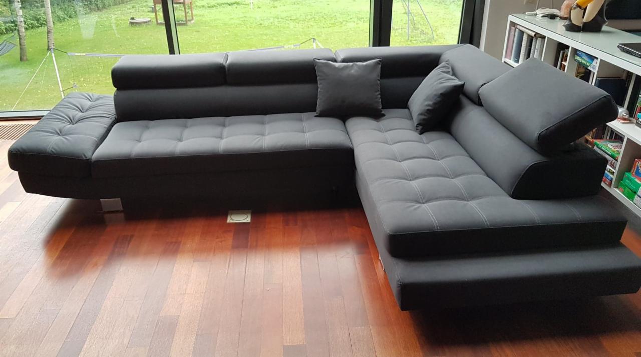 Szary narożnik tapicerowany z pikowaniem w salonie z drewnianą podłogą i dużym oknem z widokiem na zieleń.