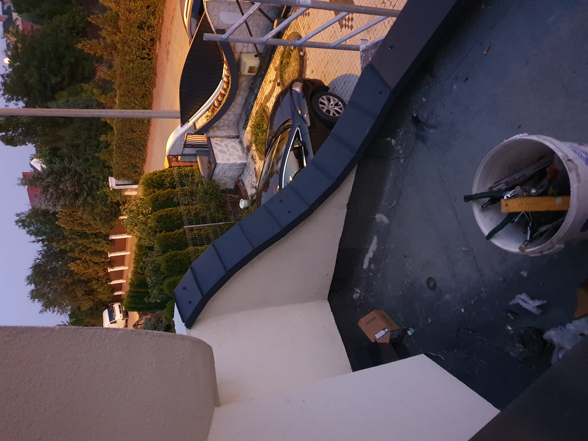 Zamontowana, ciemnoszara obróbka blacharska dachu z widocznymi elementami mocującymi; w tle budynek, zaparkowany samochód osobowy i wiadro z narzędziami.