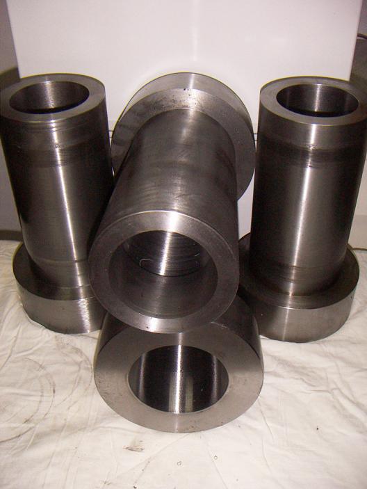 Metalowe tuleje po obróbce skrawaniem, ułożone na białym materiale, widoczne ślady po obróbce.