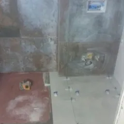 Układanie płytek podłogowych w łazience w Gniewkowie, widoczny laser krzyżowy i krzyżyki dystansowe.