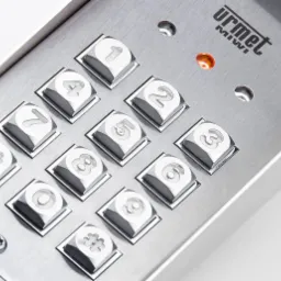 Metalowy panel domofonu z podświetlanymi przyciskami numerycznymi i logiem Urmet Miwi, widoczne ślady użytkowania.