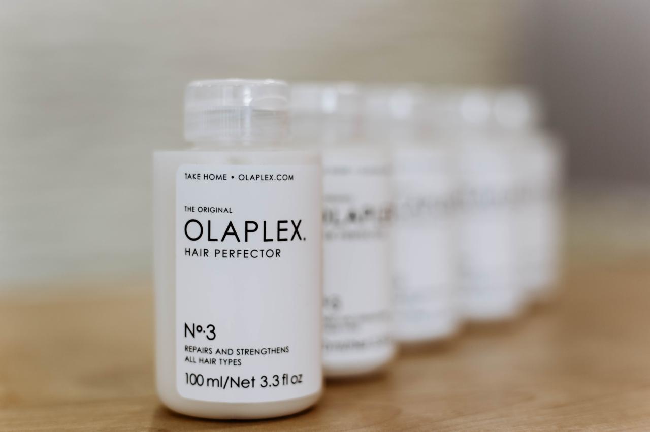 Rząd białych butelek Olaplex No. 3 Hair Perfector na drewnianej powierzchni, z etykietami skierowanymi do przodu i rozmyciem tła.